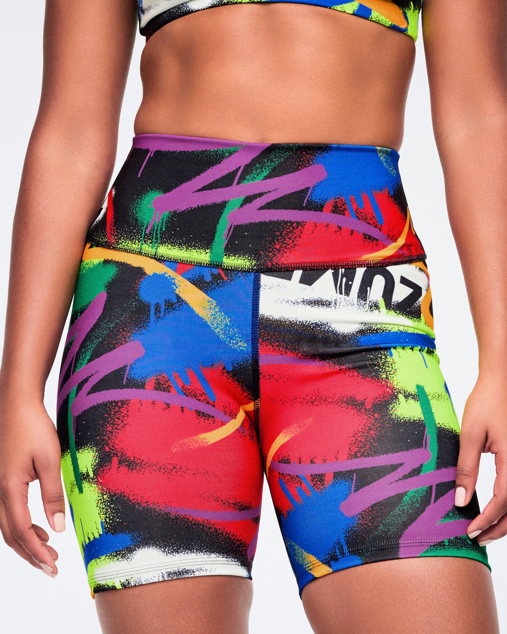 Female model wearing colorful athletic biker shorts with abstract design on a plain white background.