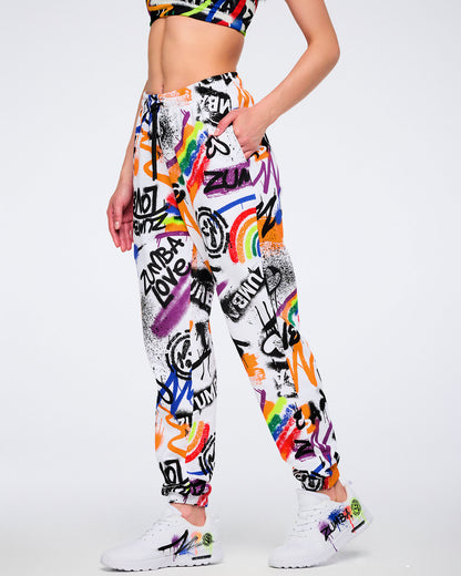 Female model wearing white and colorful graffiti-style pants with her hand in the left pocket and visible drawstring wearing matching graffiti-style shoes against a white background.