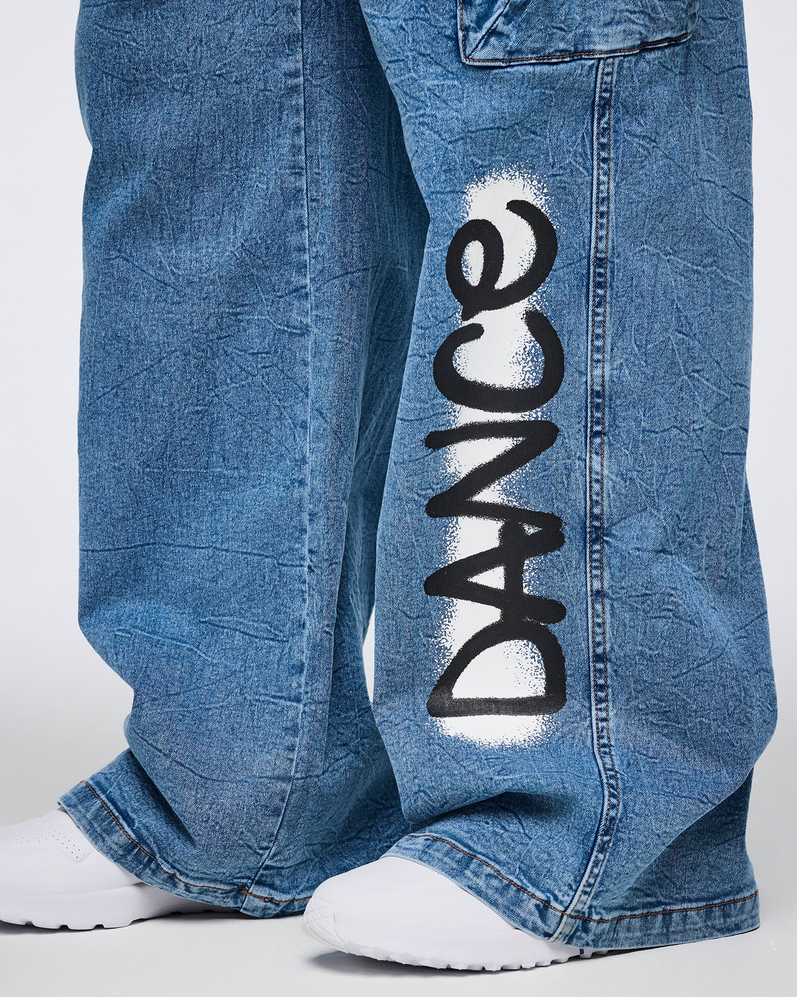 Female model wearing denim cargo pants with a close-up of the 'DANCE' spray-painted on the leg against a white background.