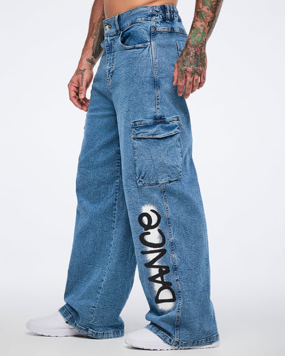Male model side view in denim cargo pants with “DANCE” on the left leg and cargo pocket against a white background.