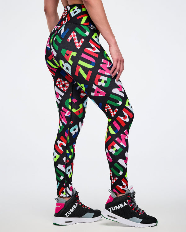 Side and partial back view of a female model wearing leggings with colorful Zumba flag-like pattern on a white background.