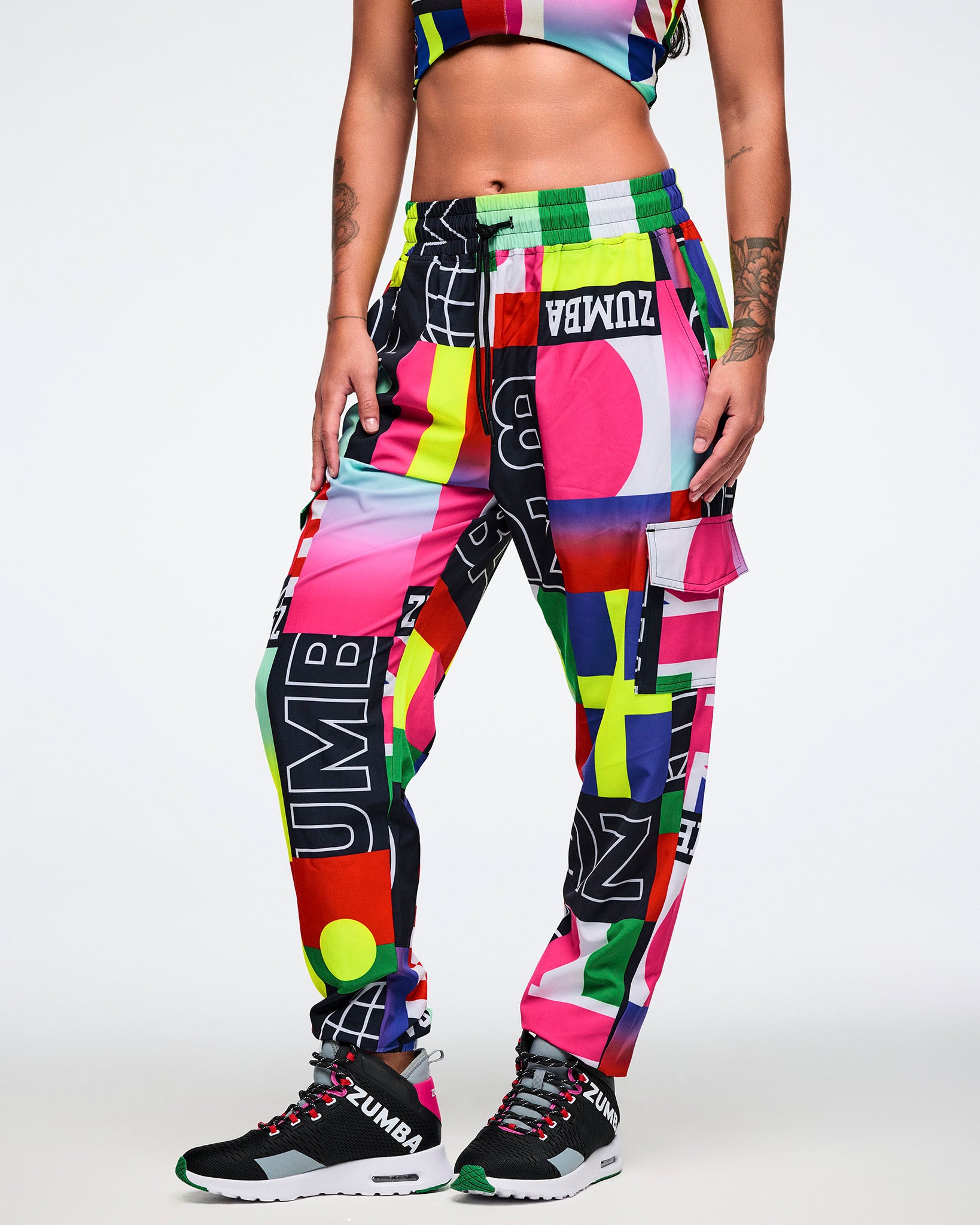 Female model wearing colorful Zumba pants and bra on a white background.