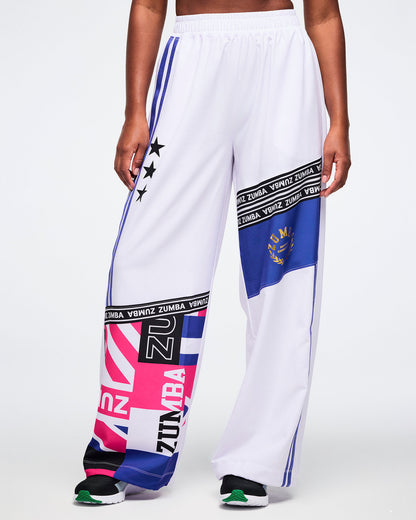 Close view from the front of a female model wearing white Zumba pants with colorful patterns and branding on a white background.