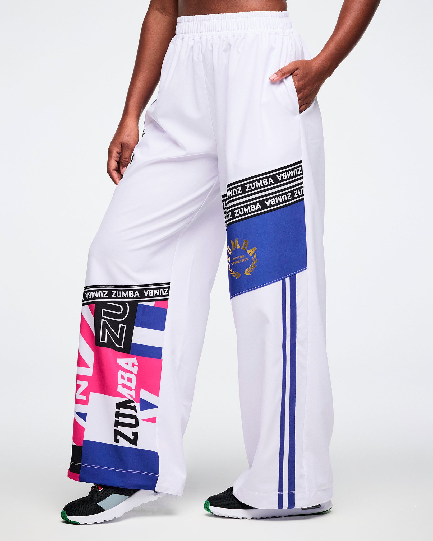 Female model in white pants with colorful Zumba branding on a white background.