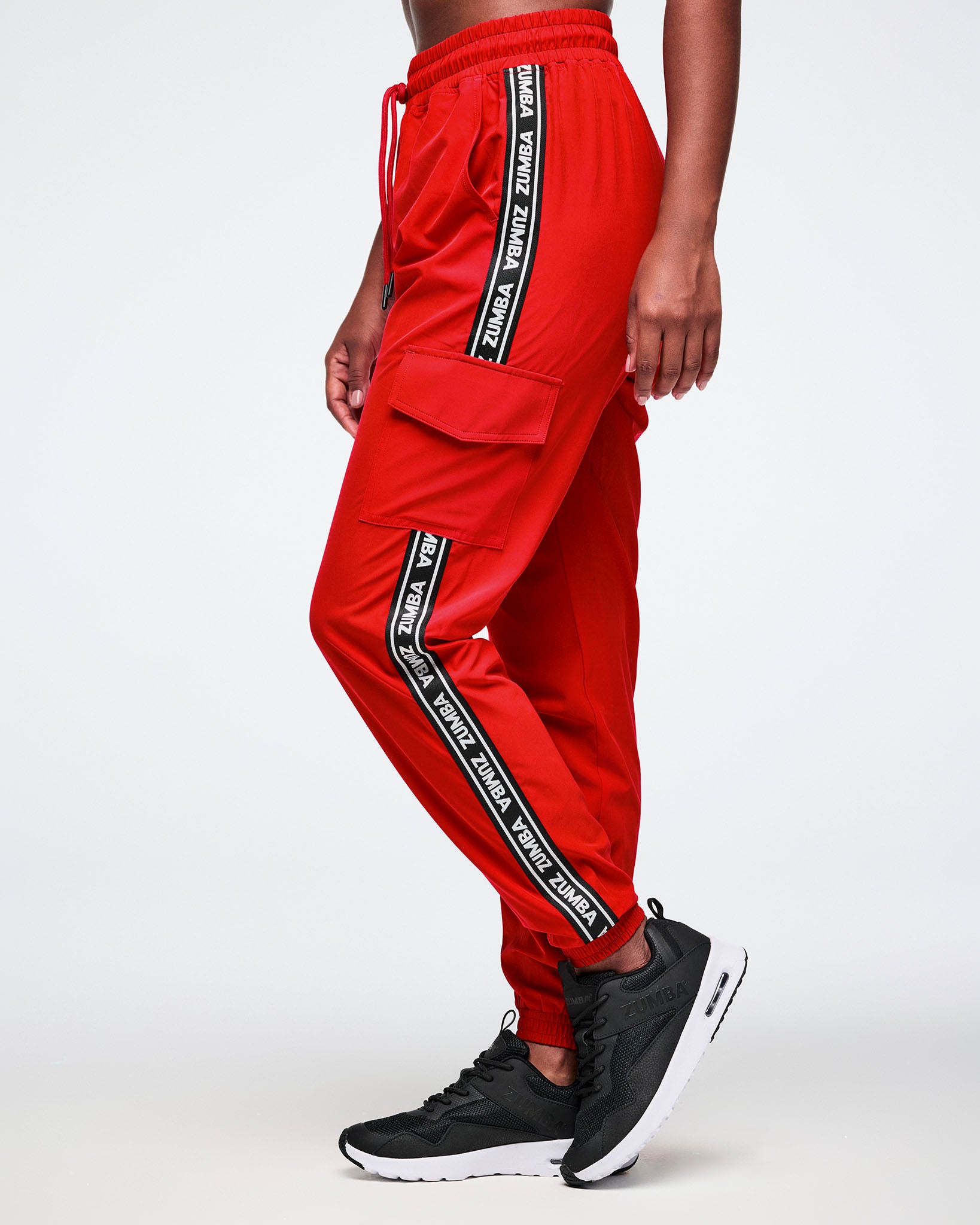 Female model wearing red cargo pants with black and white stripes saying 'Zumba' in white on a white background.