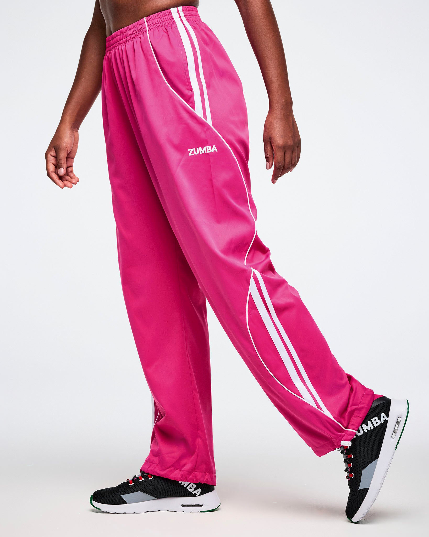 Female model wearing pink Zumba pants with white stripes on a white background.