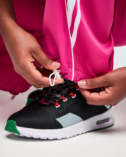 Close-up of bright pink pants with adjustable cuffs in use, paired with a black Zumba athletic shoe on a white background.