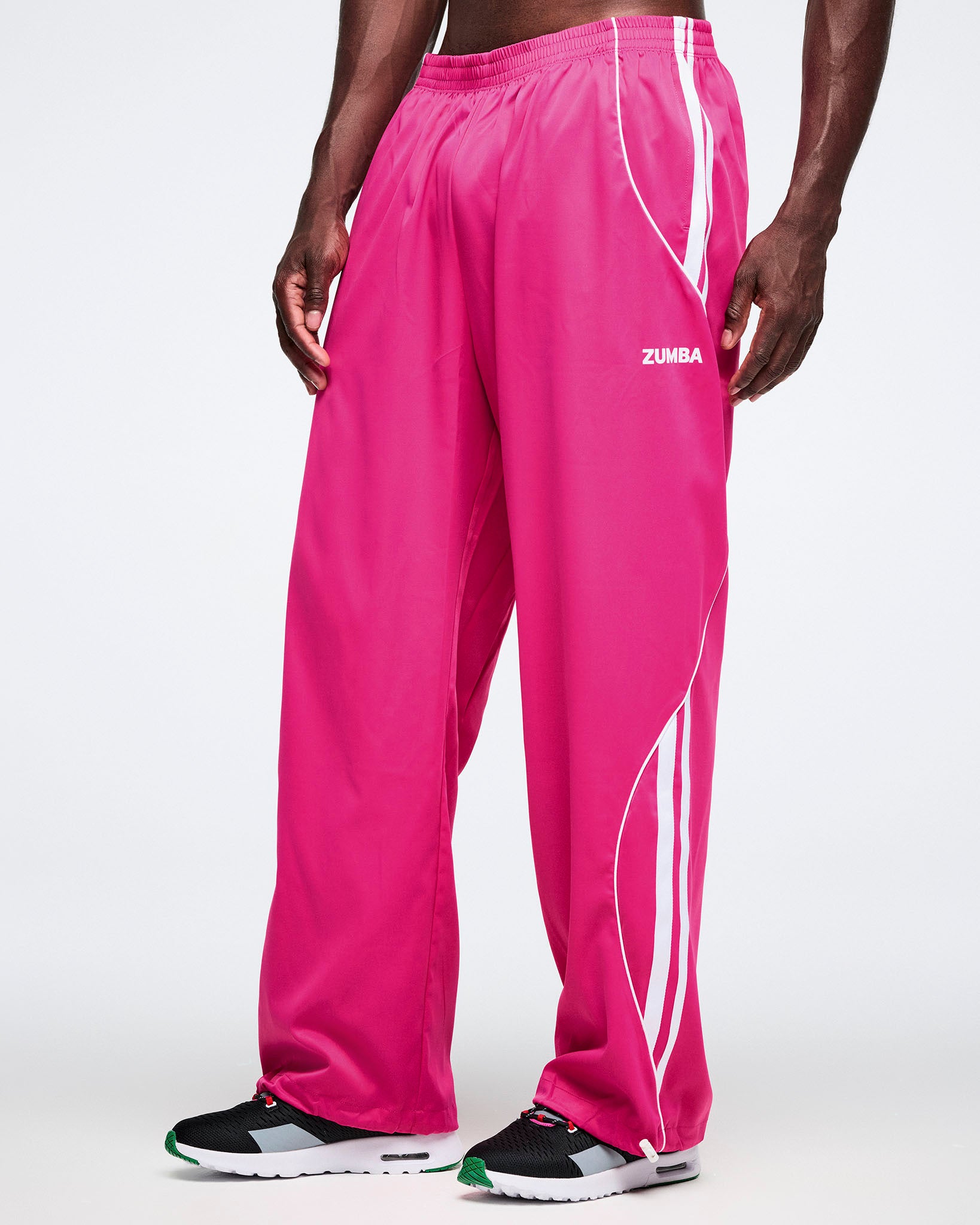 Male model wearing pink Zumba pants with white stripes on a white background.