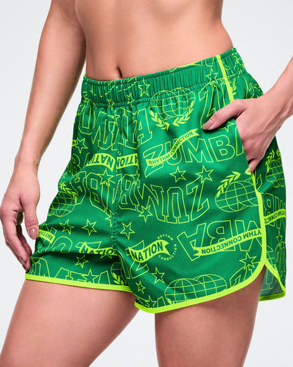 Female model wearing green athletic shorts with neon yellow accents and text on a white background.