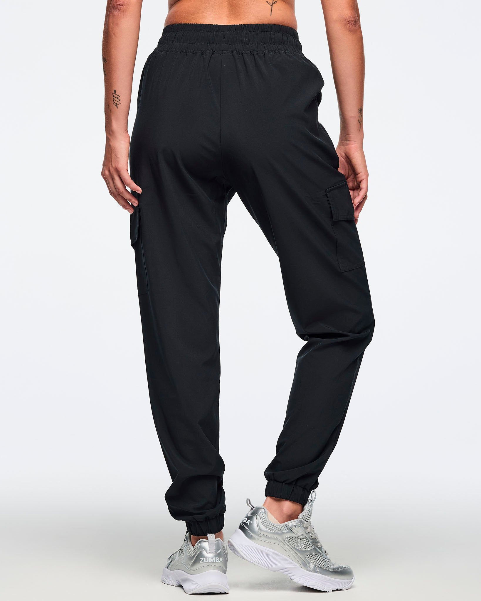 Black jogger pants shown from the back with an elastic waistband, cargo pockets, and tapered cuffed ankles. Female model is wearing the relaxed-fit joggers with silver athletic sneakers.