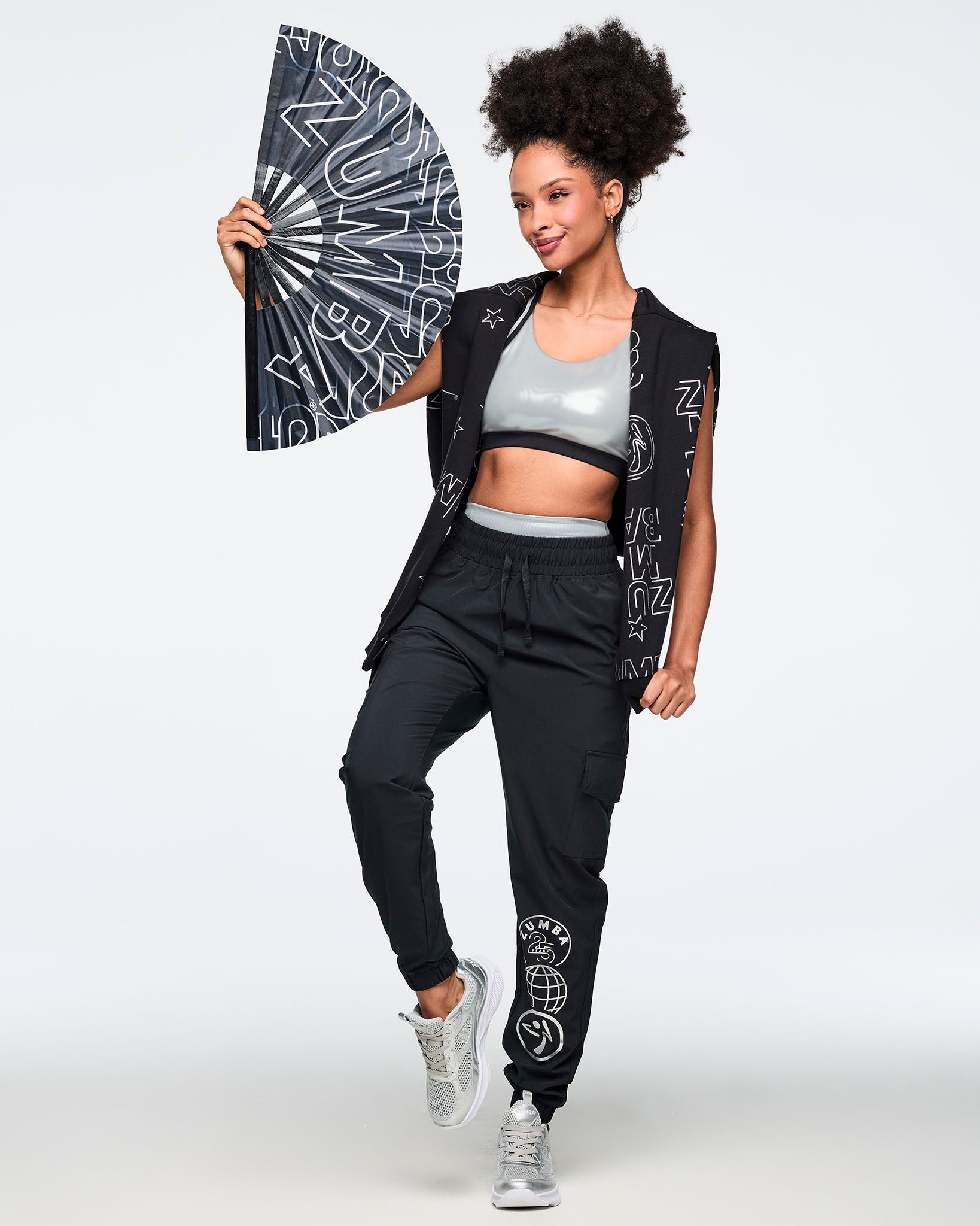 Black jogger pants with an elastic drawstring waistband, cargo pockets, and tapered cuffed ankles. Female model is wearing the relaxed-fit joggers with a silver sports bra, a black sweatshirt wrapped around her shoulders, and silver athletic sneakers.