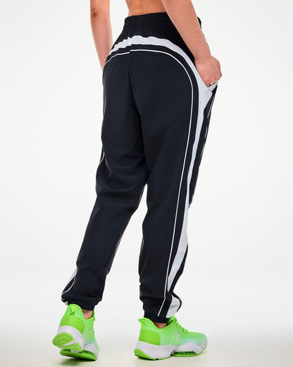 Shown from the back, female model wearing black joggers with a white side stripe, hand in side pocket.