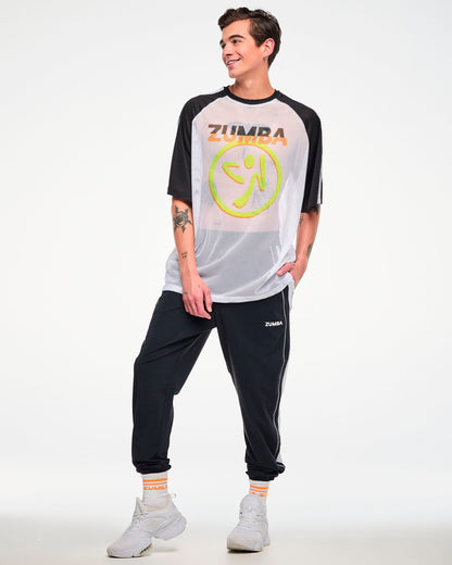 Male model, full view, wearing a white and black mesh tee with a yellow Zumbito logo, and "ZUMBA in black and orange text, paired with black joggers and white shoes.