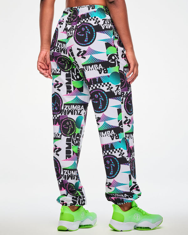 Back view of a female model wearing white track pants with an all-over abstract print, paired with green sneakers.