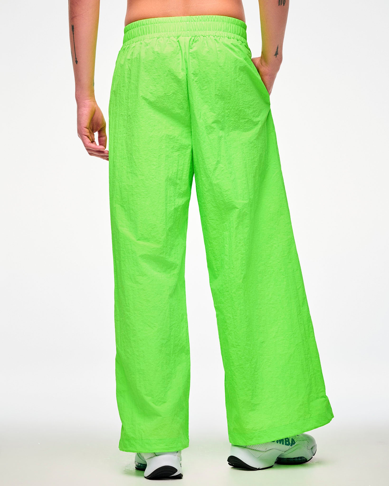 Shown from the back, male model wearing green wide-leg track pants and white shoes, hand in the side pocket.