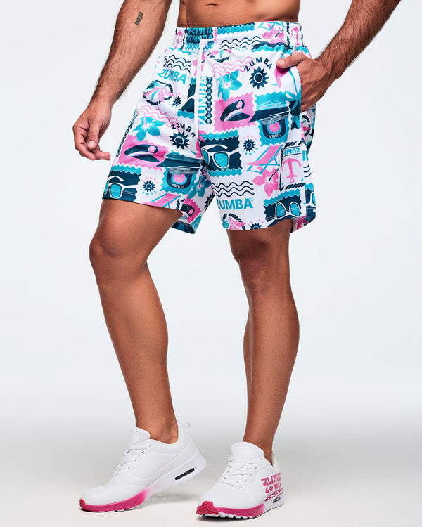 White elastic-waist drawstring shorts with a teal-and-pink allover Zumba beach print and loose fit; shown on a male model with white sneakers with hot-pink soles.