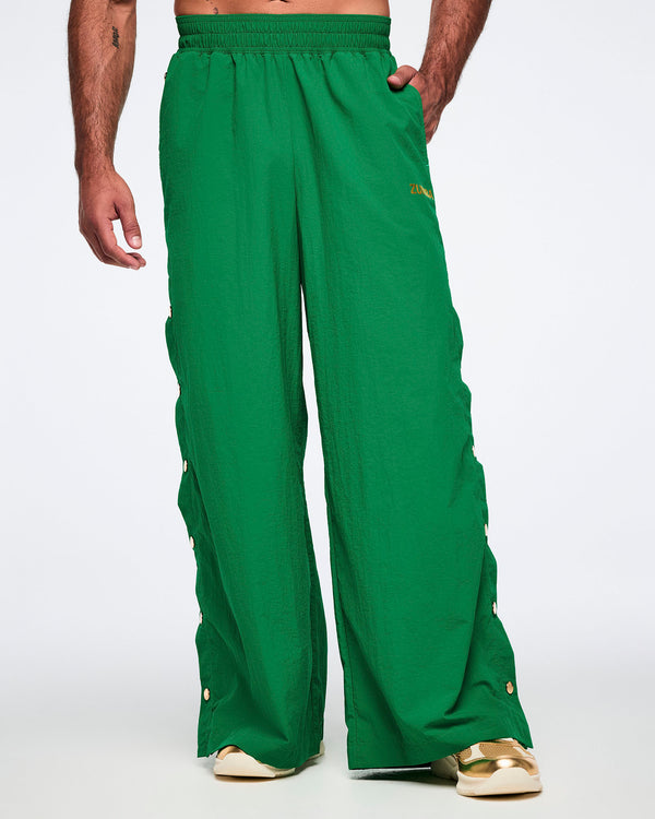 Male model wearing green wide-leg pants worn by a person in golden shoes on a white background.