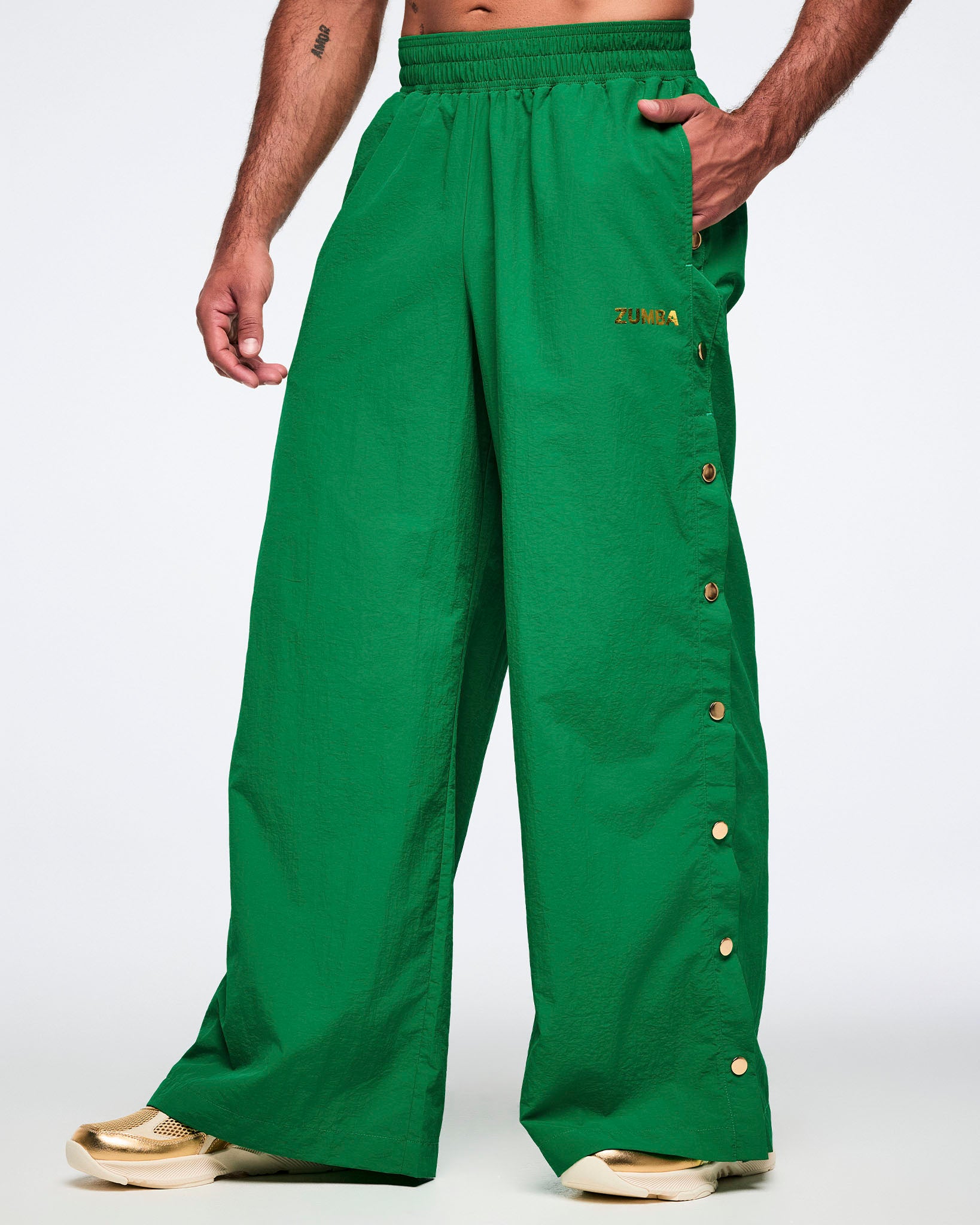 Male model wearing green wide-leg pants with gold buttons on a white background.