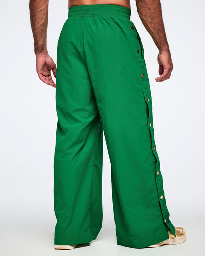 Back view of a male model wearing green wide-leg pants with gold buttons on a white background.  