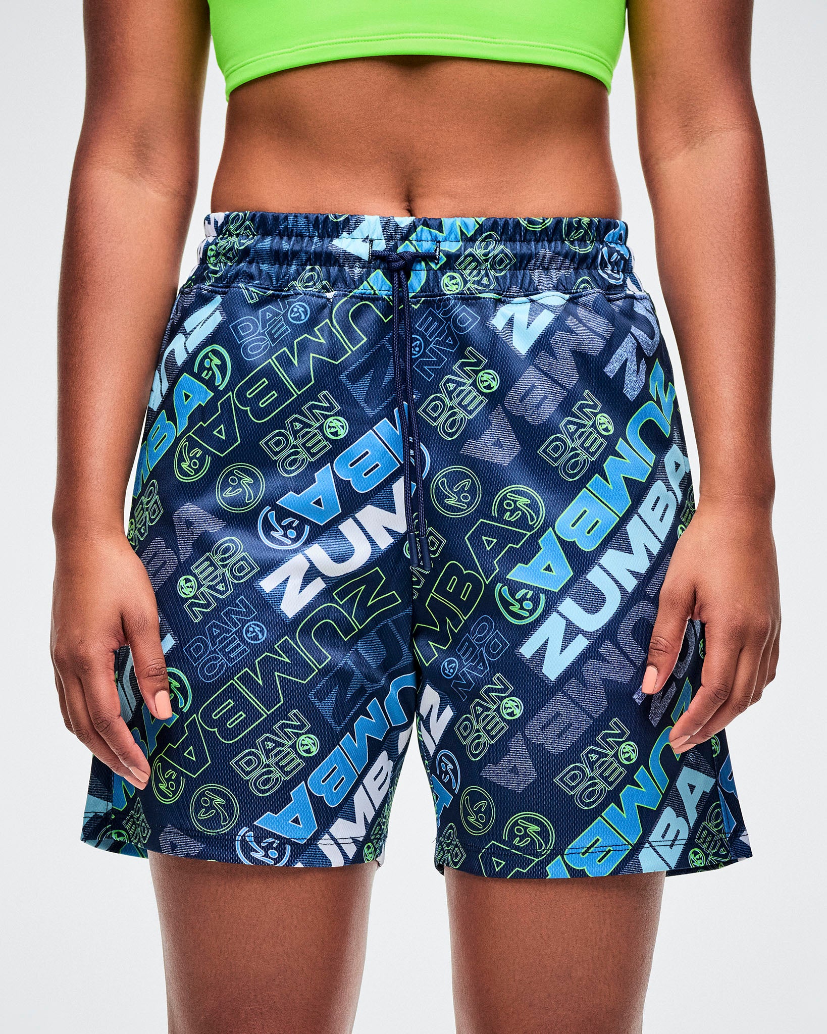 Female model wearing blue patterned Zumba shorts with brand logo on a white background.