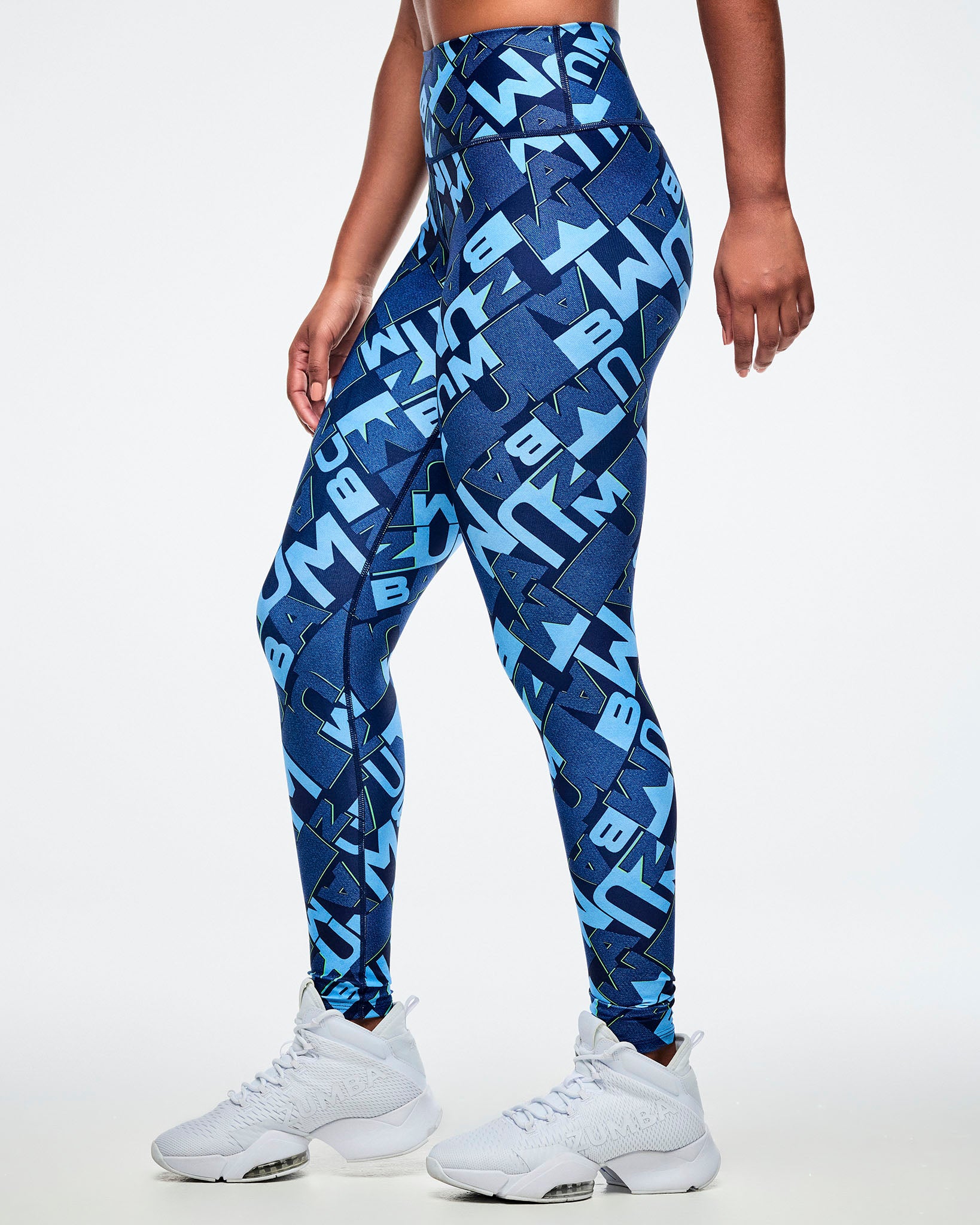 Side view of a female model wearing blue patterned leggings with white sneakers on a light gray background.