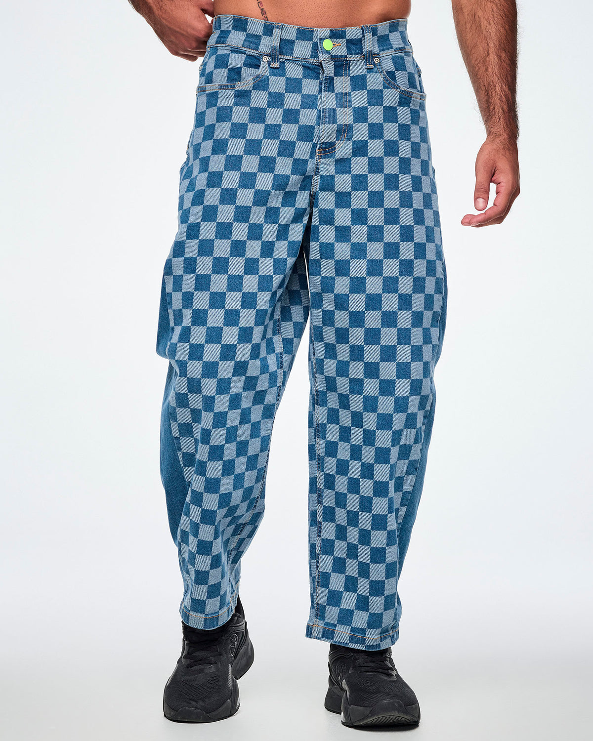 Male model in denim barrel ankle pants with a light and medium blue checkerboard pattern, a lime green front button and paired with black shoes.