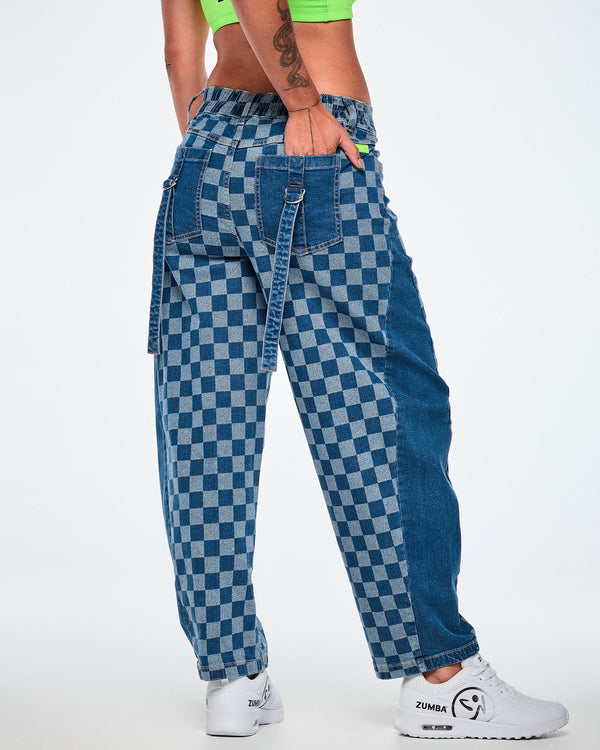 Shown from the back, a female model in the barrel ankle pants with a hand in the back pocket, showing the elastic waistband, straps with silver D-rings on the back pockets, and the rounded barrel legs, all paired with white shoes.