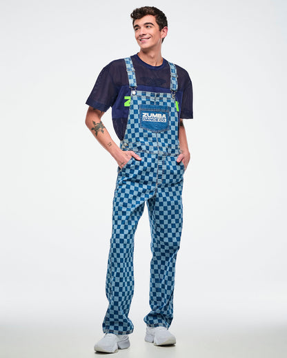 Male model wearing checkered denim overalls layered over a blue mesh top, posing with hands in his pockets against a white background.