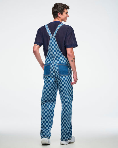 Back view of male model wearing checkered denim overalls layered over a blue mesh top, posing against a white background.