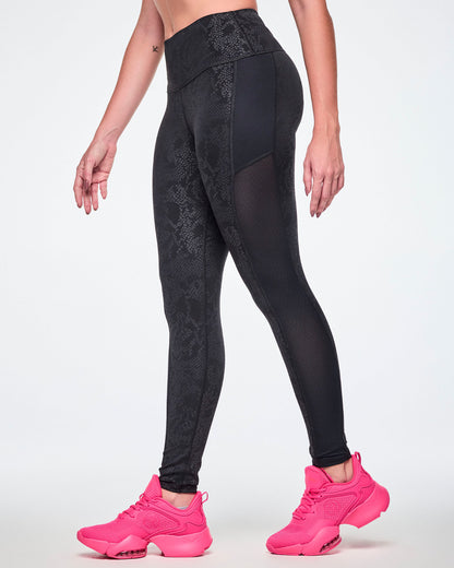 A female model wearing black high-waisted leggings with a subtle tonal snake-skin pattern and sheer mesh side panels, paired with pink shoes.