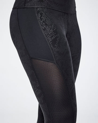 Close-up of black textured leggings with a snakeskin pattern and sheer mesh side panels, shown on a female model.