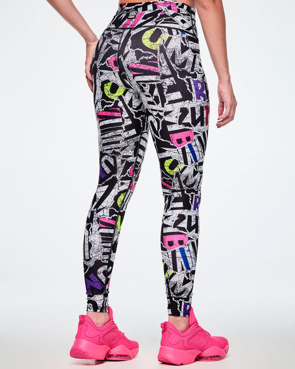 Back view of a female model wearing high-waisted leggings with a bold multicolor graffiti-style print featuring black, white, purple, blue, red, and pink lettering, paired with bright pink shoes.