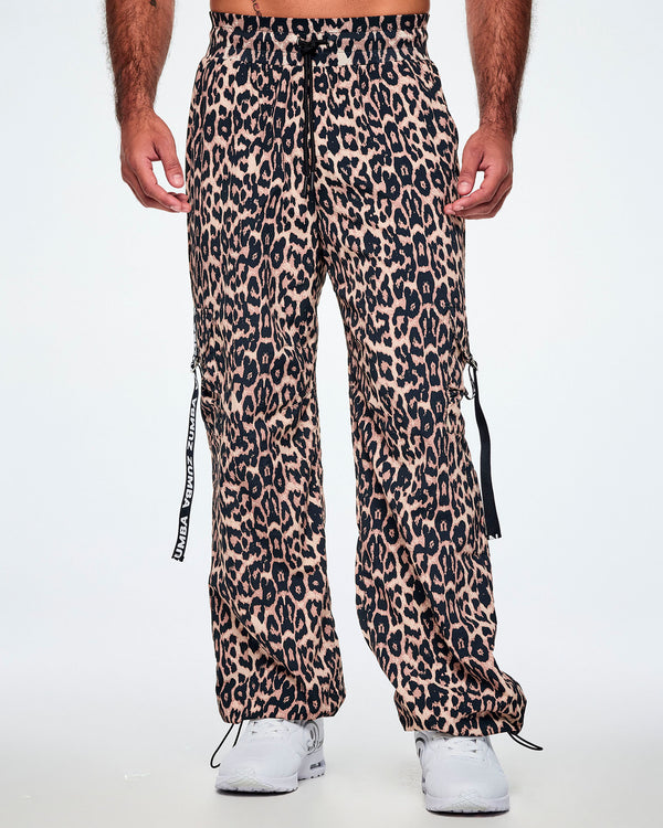 Front view of a male model wearing tan leopard print cargo pants with black Zumba straps on the pockets, paired with white shoes.