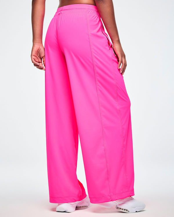 A female model shown from the back wearing pink slouch pants and white shoes, against a white background.