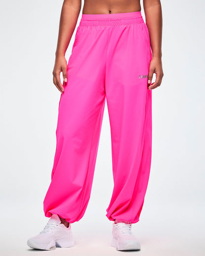 Pink slouch pants with a small silver 'ZUMBA' text on the left leg, worn by a female model, paired with white shoes.