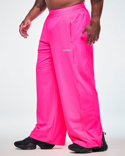 Side view of pink slouch pants worn by a male model, showing the elastic waistband, side pockets, and a small silver ZUMBA text on the upper left thigh.