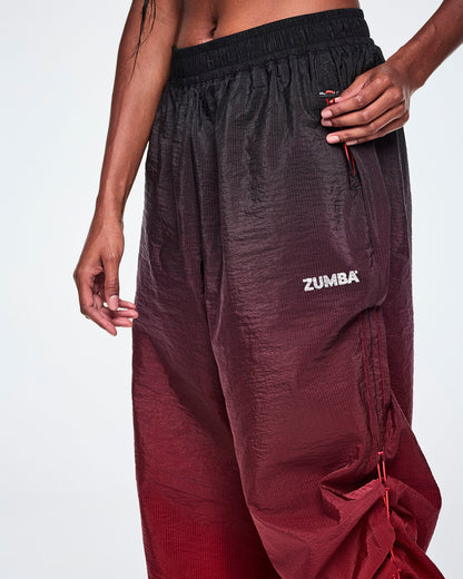 A close-up of a female model pulling on the bungee cord toggle in the pocket to adjust length of black to red gradient pants.