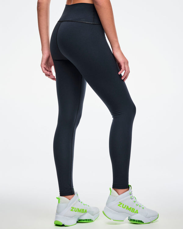 Back view of a female model wearing black Zumba leggings paired with green-and-white shoes.