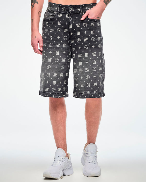 Male model wearing black denim jorts with one hand in the front pocket and featuring patterned ZW, “01,” stars, dots, and Zumbito motifs, paired with white shoes.