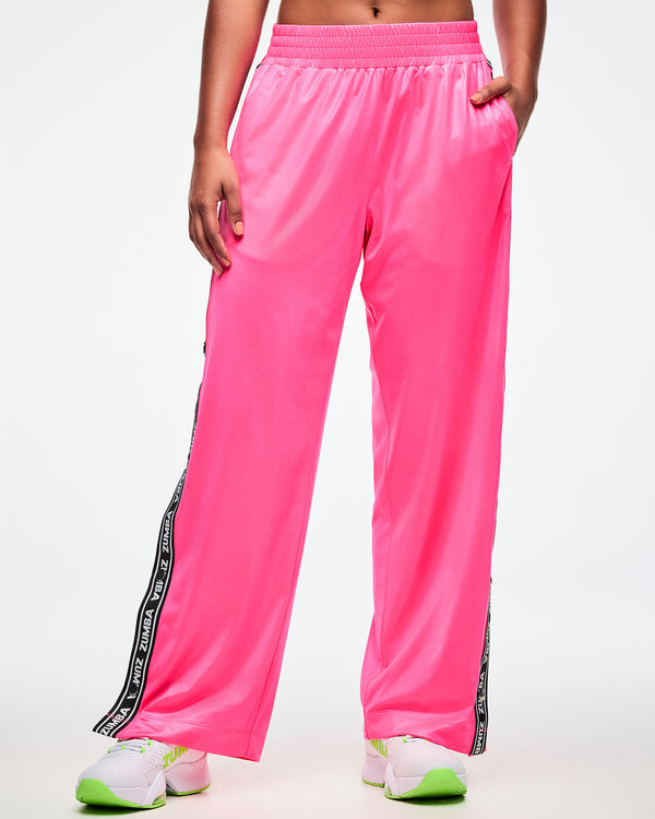 Front view of a female model wearing pink track pants with her left hand in her pocket on a white background.