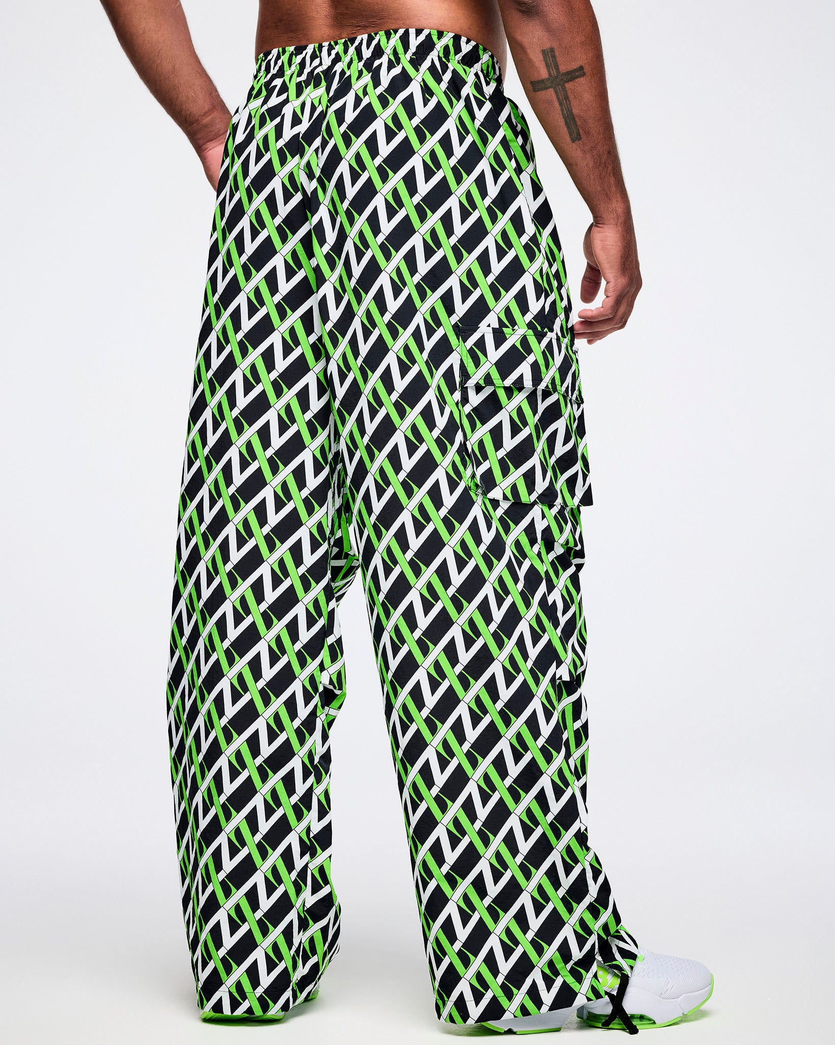 Back view of a male model wearing black cargo pants with an allover black, white and green “Z” crisscross pattern, left hand in his pocket, paired with black-and-white shoes.