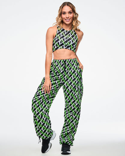 Female model wearing cargo pants with an allover black, white and neon green “Z” crisscross pattern, left hand in her pocket, paired with matching crop top and black-and-white shoes.