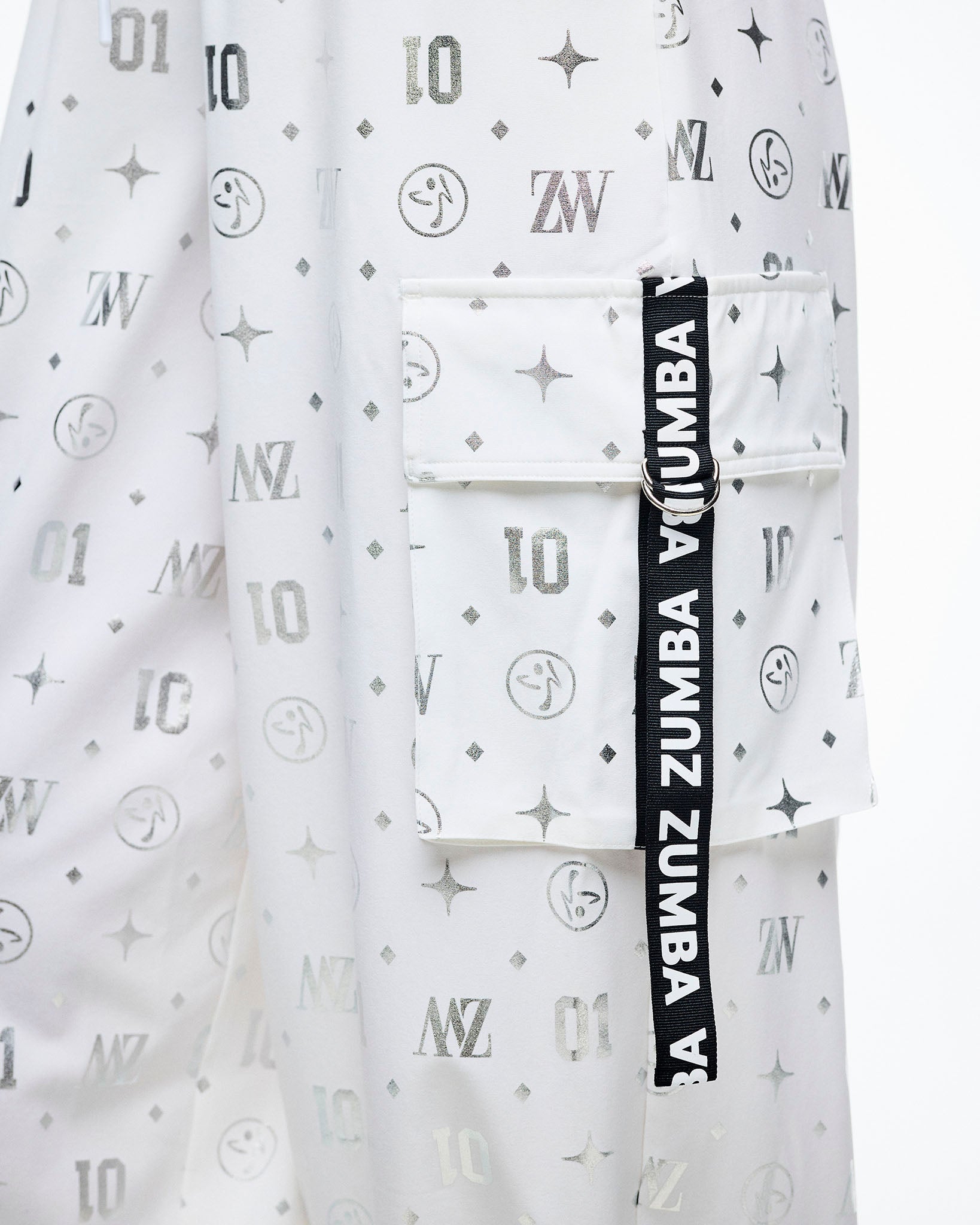 Close-up of the cargo pocket with a black‑and‑white “Zumba” ribbon, set against the silver Zumba motif print.