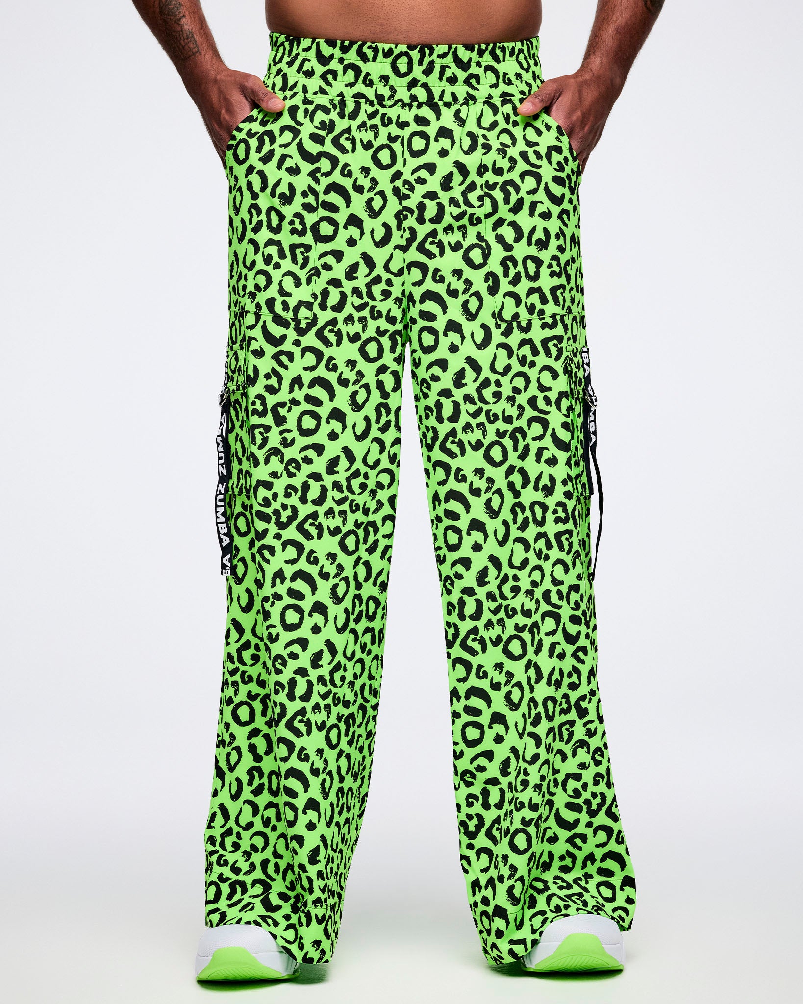 Male model wearing neon green leopard print cargo pants with hands in both side pockets.