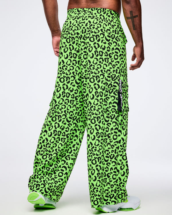 Back view of a male model wearing bright green leopard print pants with a visible brand logo on a white background.