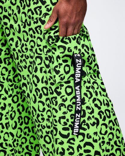 Close-up of neon green leopard-print Zumba cargo pants, hand tucked into the cargo pocket. A vertical black tag along the pocket reads “Zumba" multiple times.