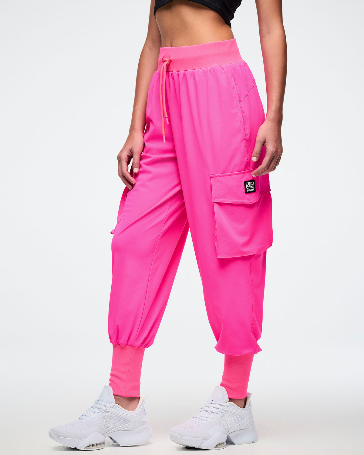 Female model wearing bright pink cargo pants showing off the left cargo pocket with black and white Zumba badge.