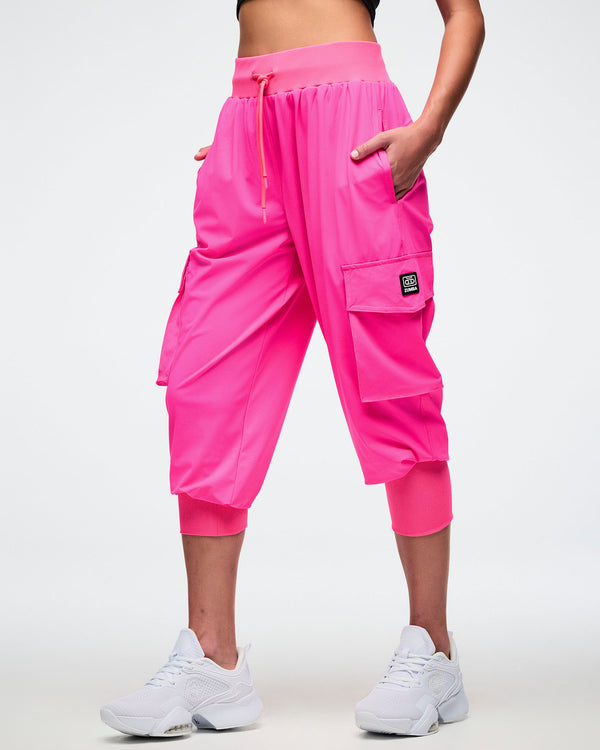 Female model wearing bright pink cargo pants with hands in her pockets and paired with white shoes.