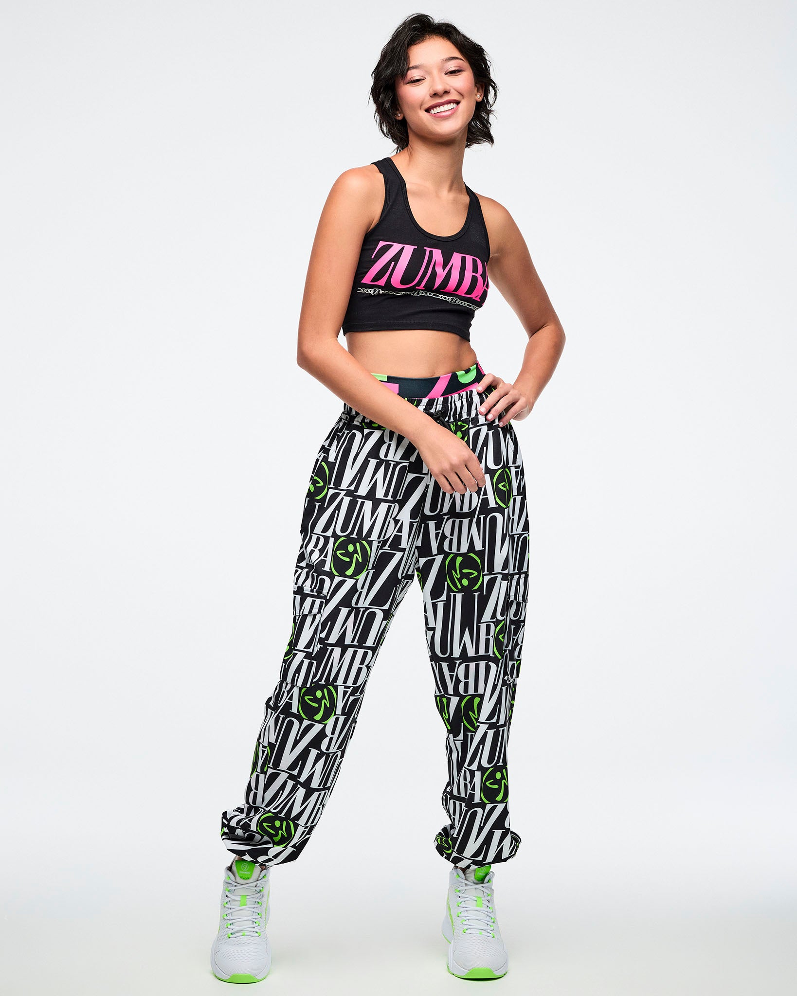 Female model wearing a Zumba branded top and black and white pants with green Zumbito accents on a white background.