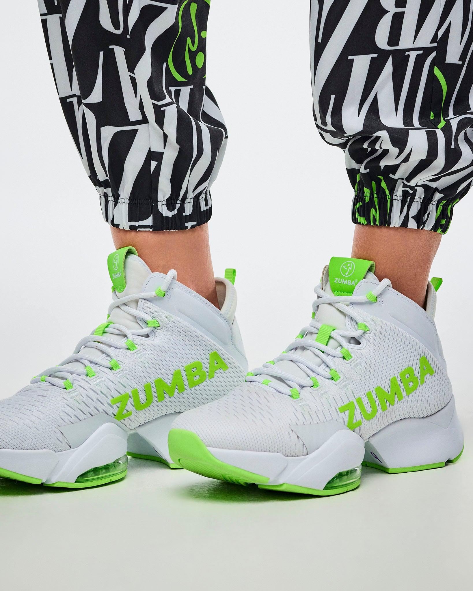 Close-up of the encased elastic cuffs on black-and-white patterned Zumba pants with green Zumbito accents, paired with green-and-white shoes.